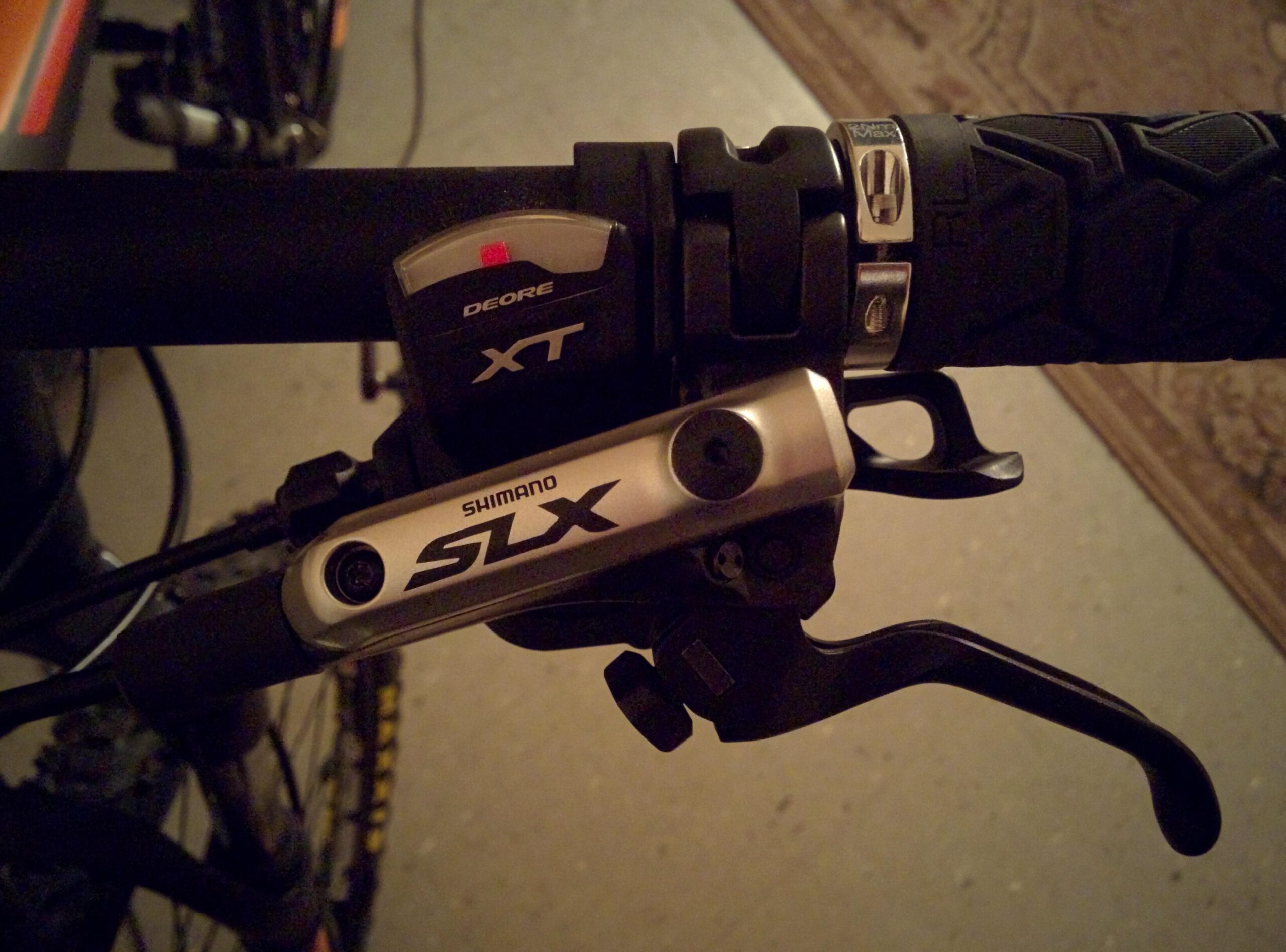 Trek Marlin 5 29er: Close-up image of a bicycle handlebar featuring Shimano SLX and XT components, including a gear shifter and brake lever, on a dark background. The handlebar grip has a textured surface for better hold.