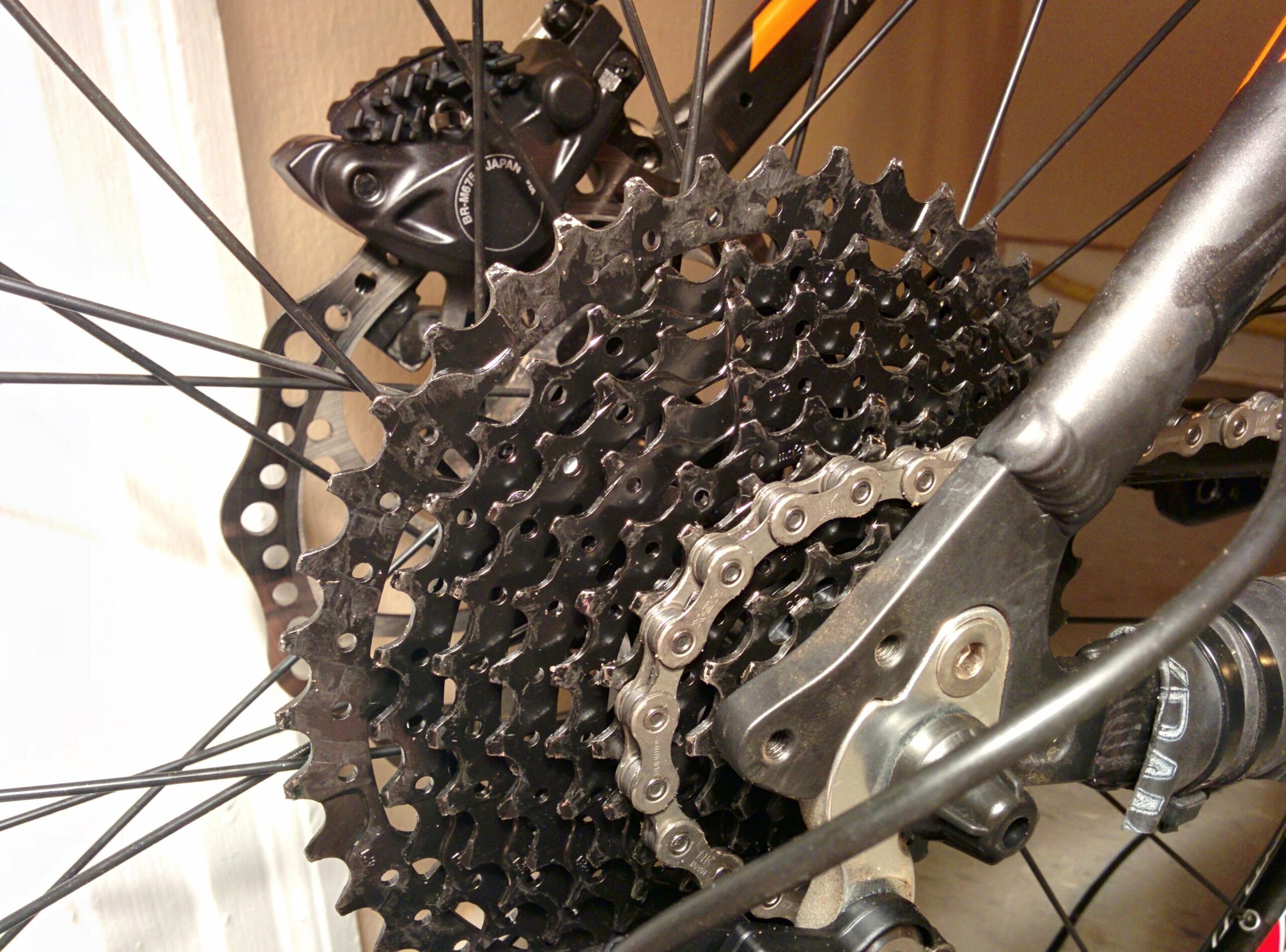 Trek Marlin 5 29er: A close-up view of a bicycle's rear cassette and chain, showcasing the detailed configuration of the sprockets and chain links. The image highlights metal components, including a black derailleur, and the intricate design of the gears.