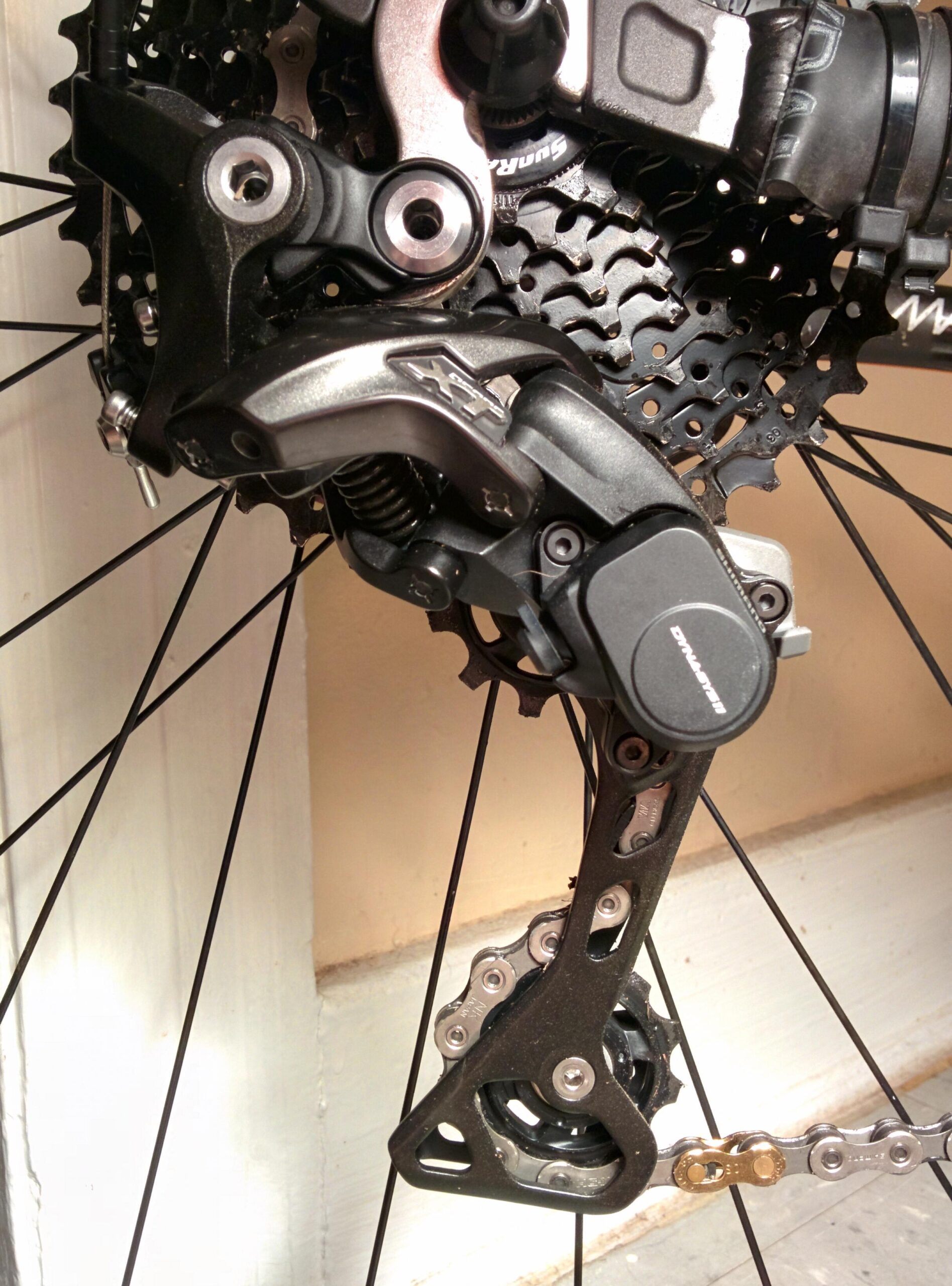 Trek Marlin 5 29er: Close-up view of a bicycle's rear derailleur mounted on a cassette, showcasing components such as the chain and gearing system. The image highlights the intricate details and mechanical design of the derailleur, including springs and adjustment features. The background is a neutral-colored wall.