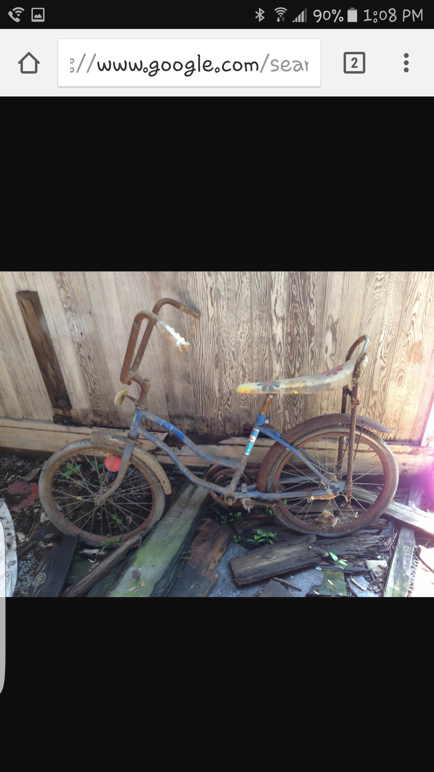 Specialized Crave Comp 29: A rusty, abandoned children's bicycle with a blue frame and faded decorative details, leaning against a wooden wall. The tires are flat and the bike is surrounded by weathered wooden planks and patches of green grass.