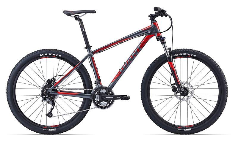 Giant Talon 27.5 3: Mountain bike with a dark gray and red frame, featuring wide tires and disc brakes, positioned on a white background.