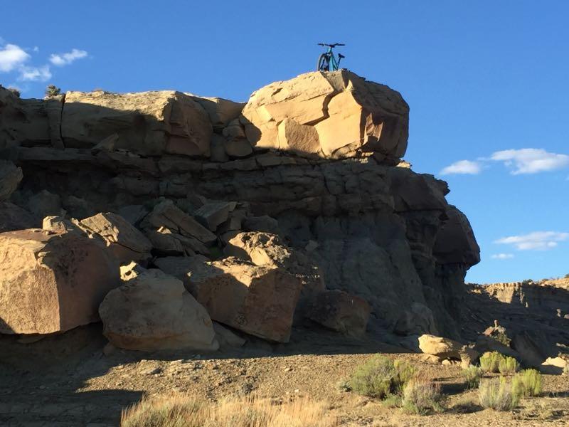 A mountain bike perched on a large rock formation overlooking a rugged landscape under a clear blue sky. High Desert Trail System mountain bike trail.