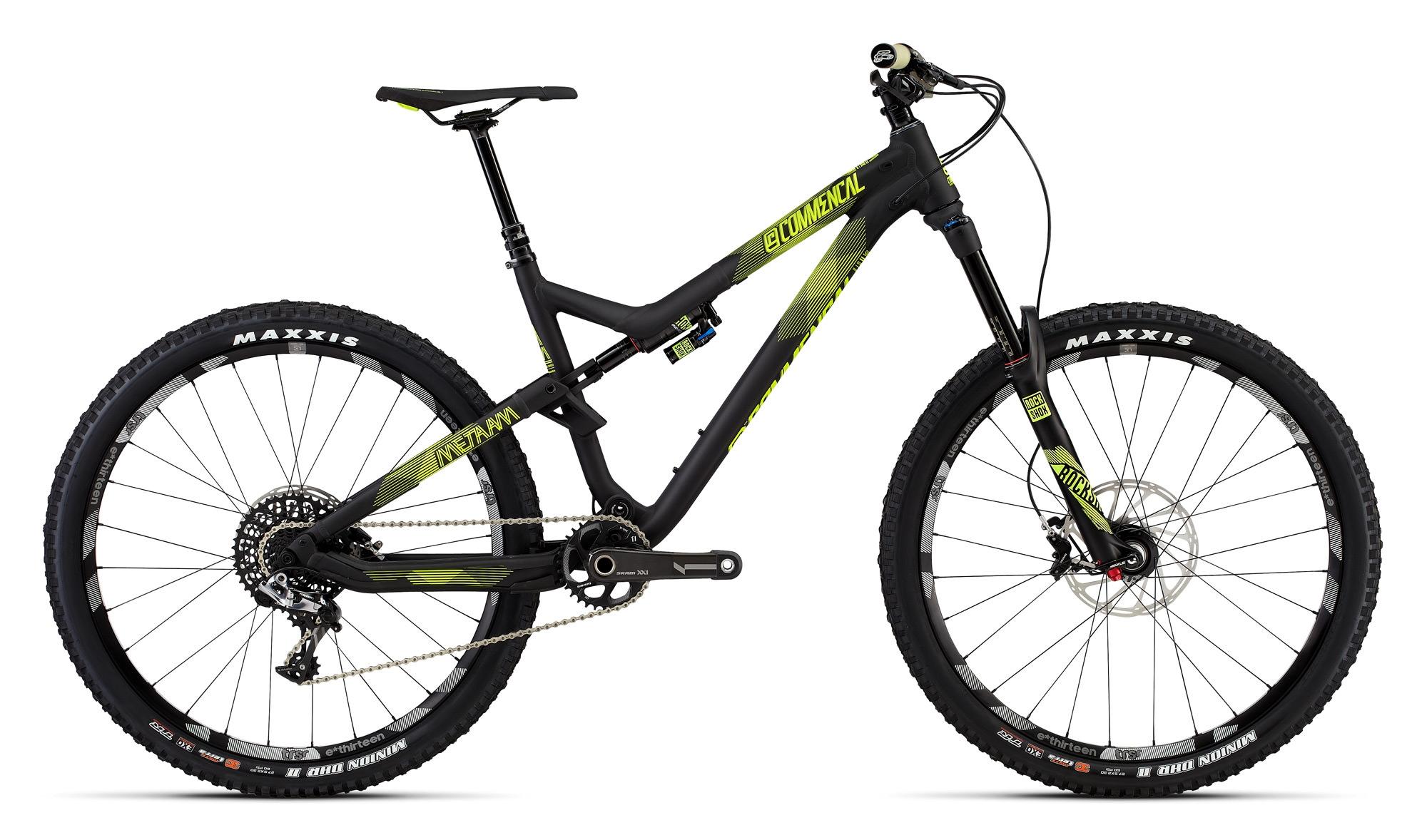 Commencal Meta AM V4: A black mountain bike with vibrant green accents, featuring wide tires and a sturdy frame. The bike is positioned at a slight angle, showcasing its front fork, gear system, and suspension components. The wheels are branded with "MAXXIS" and the bike displays the model name "METAM" prominently.