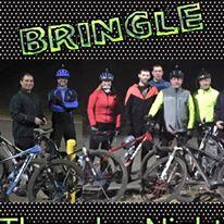 A group of seven cyclists poses together at night, wearing various cycling gear, including helmets and reflective jackets. They stand next to their mountain bikes, ready for a night ride. The background features a textured black design. Text at the top reads "BRINGLE," in bright green, while a smaller text at the bottom says "Thursday Night." Bringle Lake Mountain Bike Trail System mountain bike trail.