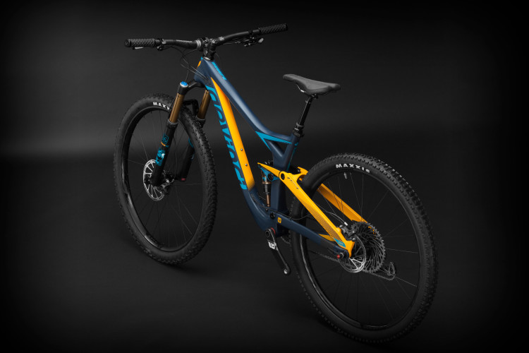 A modern mountain bike with a sleek, blue and yellow frame positioned at an angle against a black background. The bike features sturdy tires, front and rear suspension, and a prominent logo. The handlebars and seat are designed for optimal rider comfort and performance.