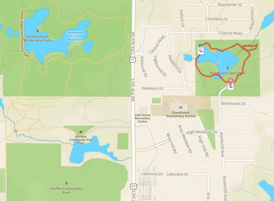 Map showing the layout of several parks, including Sutton Urban Wilderness Park, Northeast Lions Park, and Norman Community Dog Park, along with nearby streets and landmarks. The map outlines walking paths and features bodies of water within the parks. Lions Park mountain bike trail.