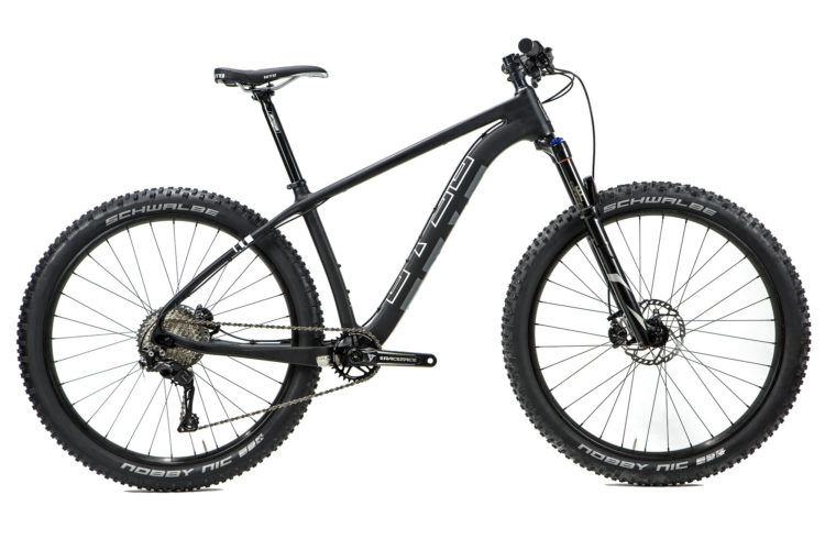 A black mountain bike featuring a sturdy frame, wide tires, and a high-performance suspension fork. The bike is equipped with disc brakes, and the tires are branded with "Schwalbe Nobby Nic." It is positioned on a plain white background, showcasing its sleek design and modern components.