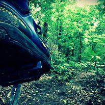 Close-up of a shoe stepping on a dirt path surrounded by lush green foliage in a wooded area. Bringle Lake Mountain Bike Trail System mountain bike trail.