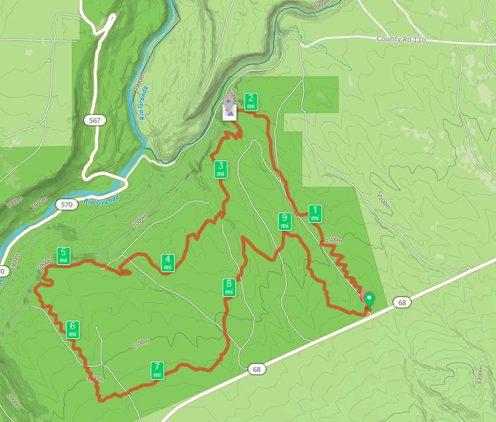 Alt tag: Map showing a hiking trail with an outlined route in red, various distance markers, and the surrounding topography of a green landscape with waterways. Taos Valley Overlook mountain bike trail.