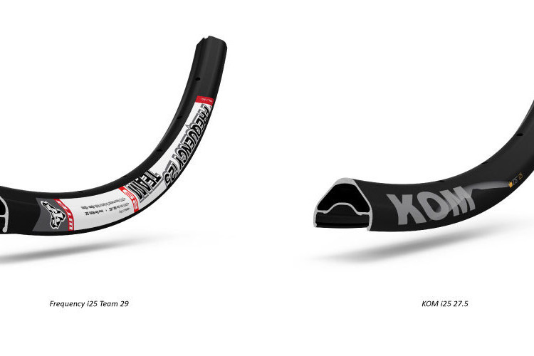 An illustration showing two bicycle rims side by side. On the left is the Frequency i25 Team 29 rim featuring a white and red design with a logo. On the right is the KOM i25 27.5 rim, characterized by a sleek black design with a bold 'KOM' logo in gray. Both rims are displayed in a curved position to highlight their profiles.
