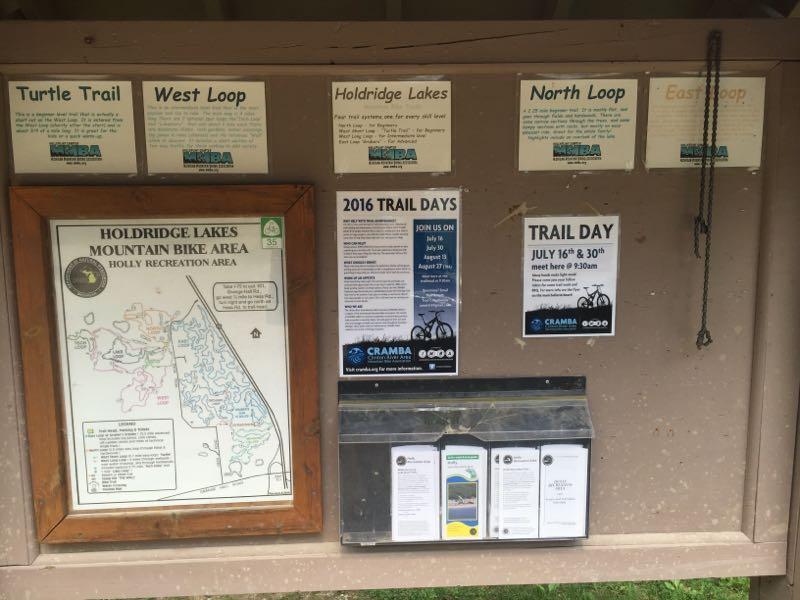Information board at the Holdridge Lakes Mountain Bike Area, featuring a map of the trails, descriptions of four biking loops (Turtle Trail, West Loop, North Loop, East Loop), and details about upcoming trail days in 2016. The board includes brochures and a box for additional informational materials. Holdridge Recreation Area mountain bike trail.