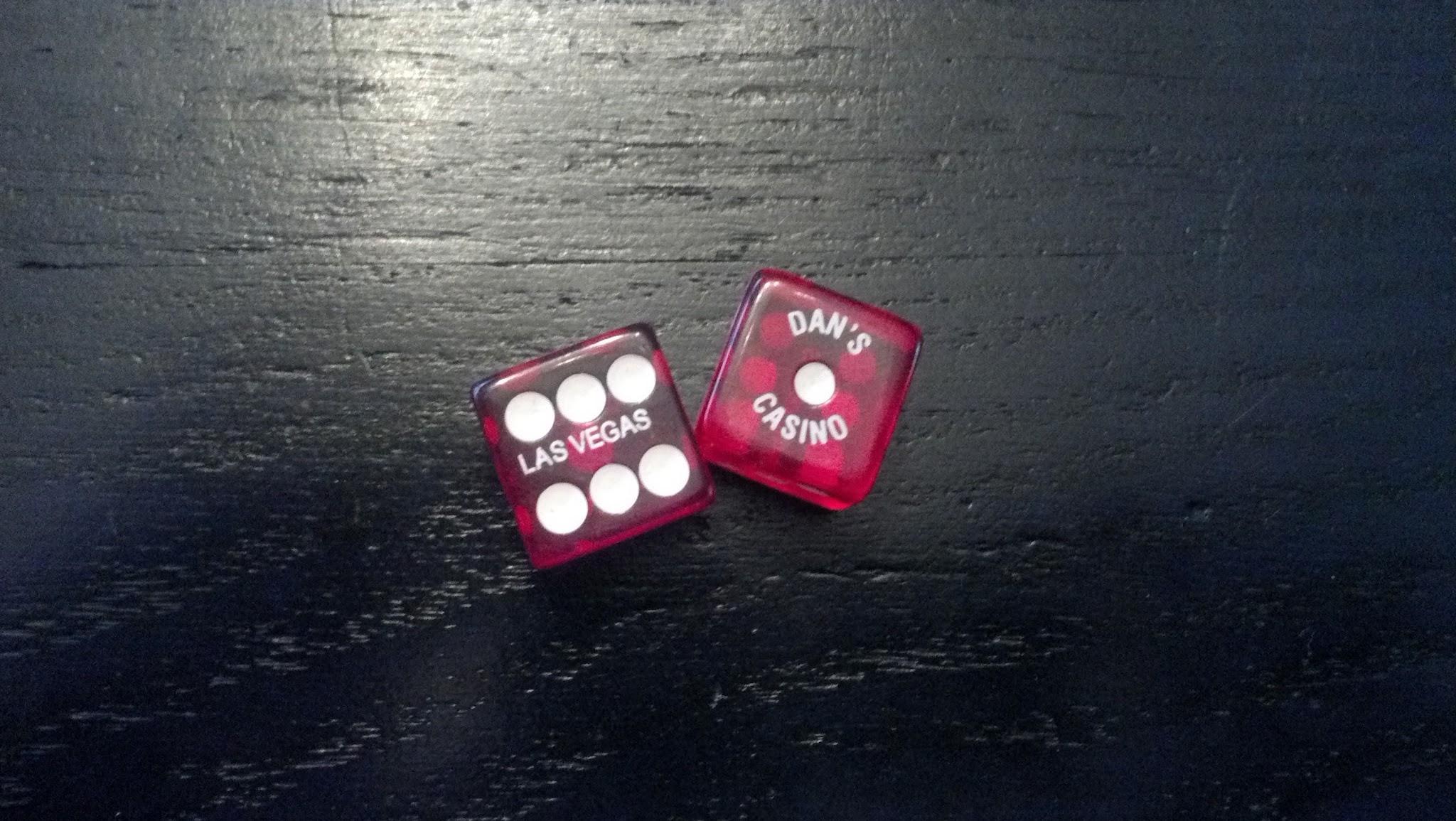 Salsa El Mariachi 3: Two red dice are placed on a black surface. One die has the text "LAS VEGAS" printed on it, while the other reads "DAN'S CASINO." Both dice show six white dots on one face.