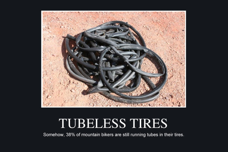 A pile of tangled black rubber bicycle inner tubes on a dirt surface, with the caption "TUBELESS TIRES" above and a humorous note about mountain bikers still using tubes below.