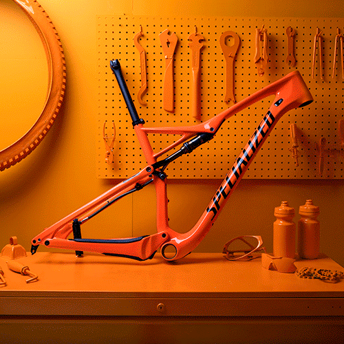 A vibrant orange bicycle frame displayed on a workbench, surrounded by various tools and equipment. The background features a pegboard with tools hanging neatly, and there are orange water bottles and goggles on the table, all set in a warm, orange-toned atmosphere.