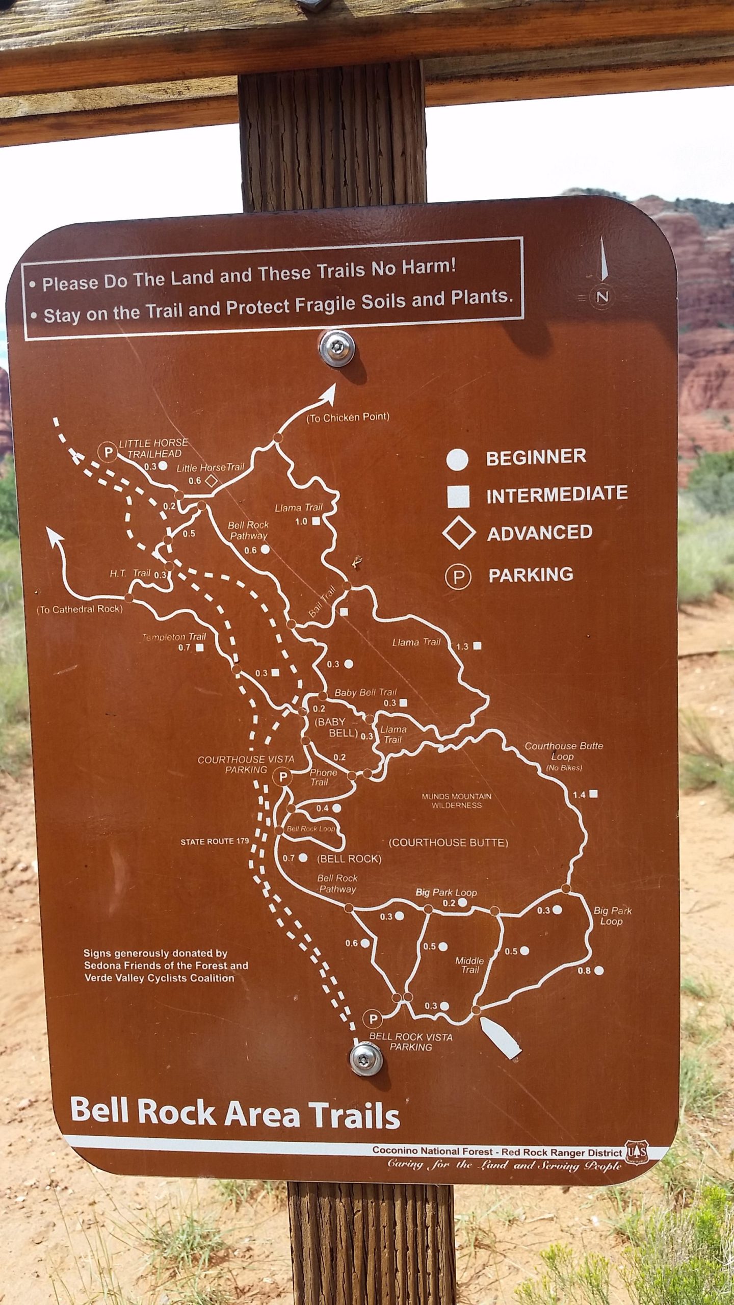 Signage featuring a map of the Bell Rock Area Trails, outlining various hiking routes labeled for beginners, intermediate, and advanced levels. The map includes notable trail names, distances, and parking areas, along with a message about protecting fragile soils and plants. The background shows a natural landscape typical of the area. Bell Rock Trailway mountain bike trail.