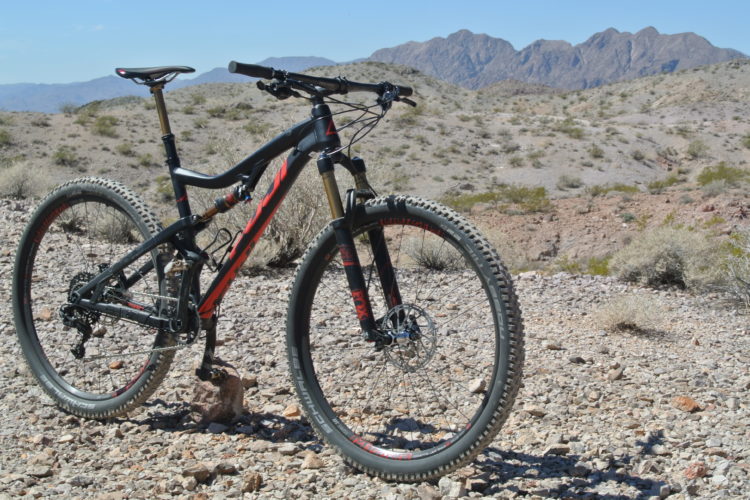 Mountain bike resting on rocky terrain with desert landscape and mountains in the background under clear blue skies.