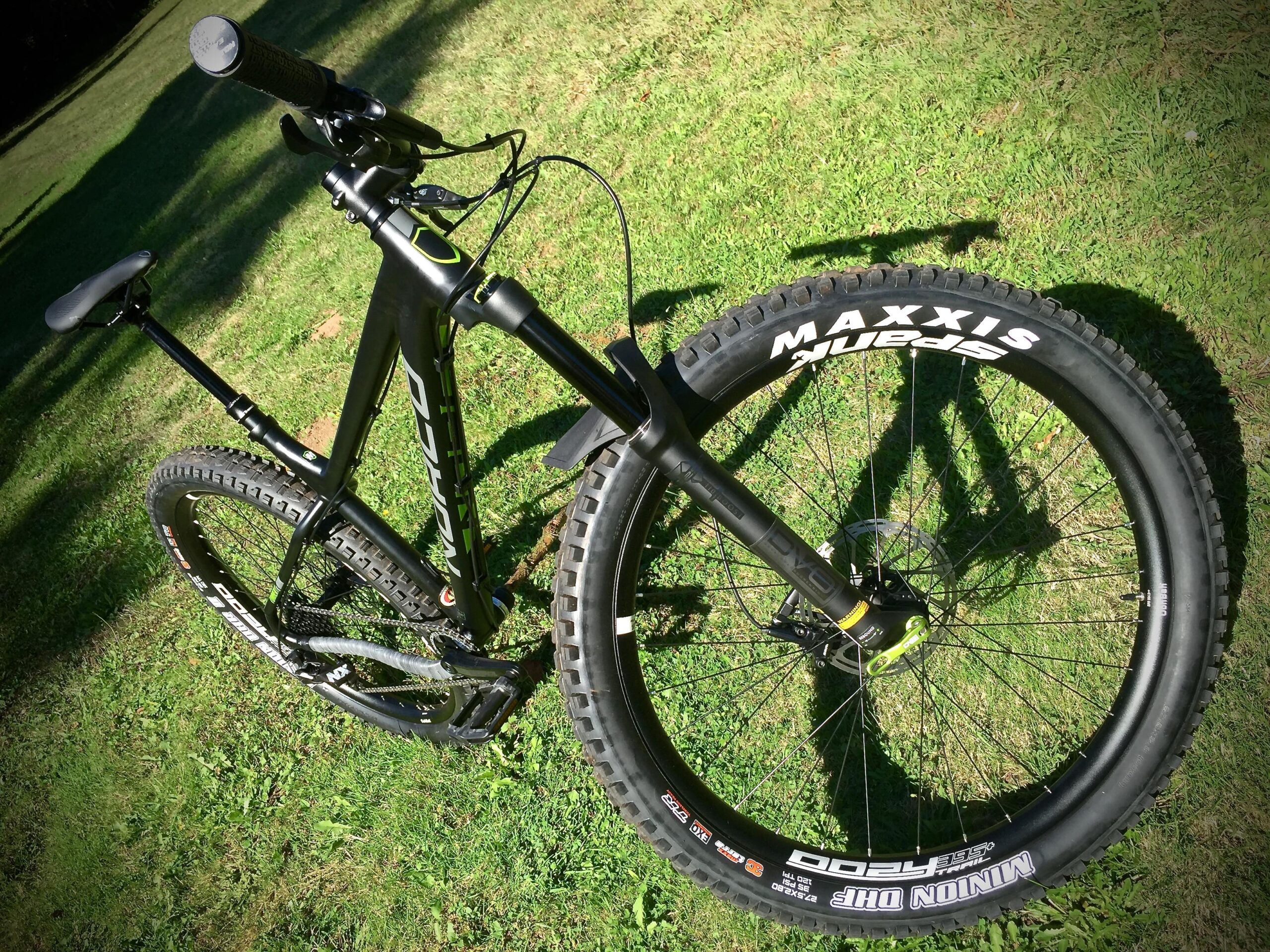 Norco Torrent 7: A black mountain bike positioned on green grass, showcasing its handlebar, seat, and wheel details. The bike features a sleek design with prominent branding on the tires and frame components, emphasizing its performance-oriented style. Shadows are cast on the grass, adding depth to the image.