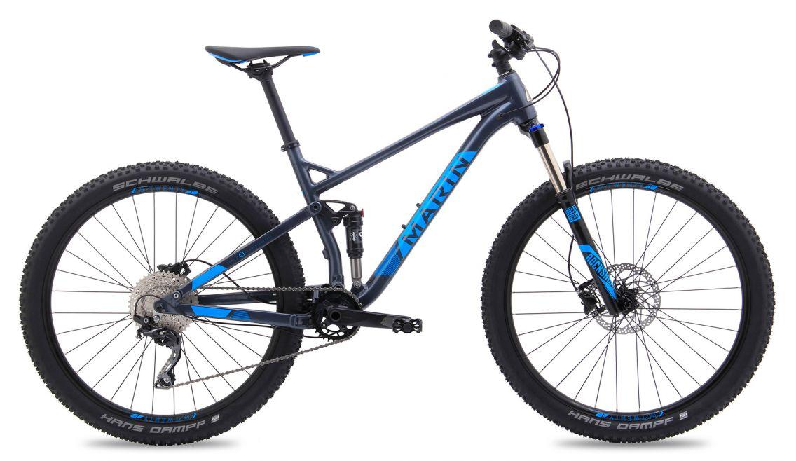 Marin Hawk Hill: A blue and gray mountain bike with a modern frame, featuring wide tires, disc brakes, and a suspension fork. The bike showcases Shimano gear components and is positioned upright against a plain background.