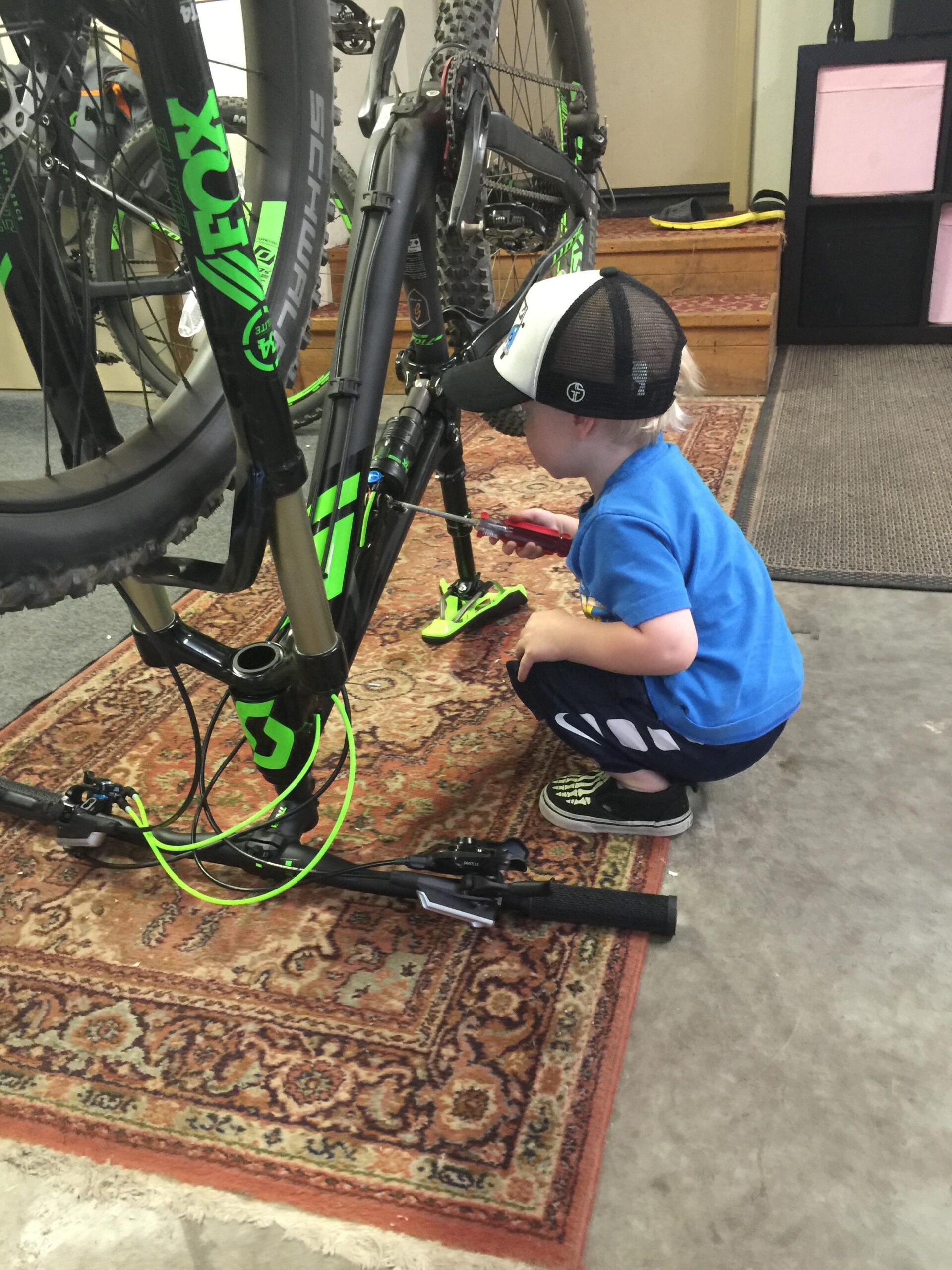 Scott Genius 910: A young child crouches next to a mountain bike, holding a small tool as they inspect and work on the bike