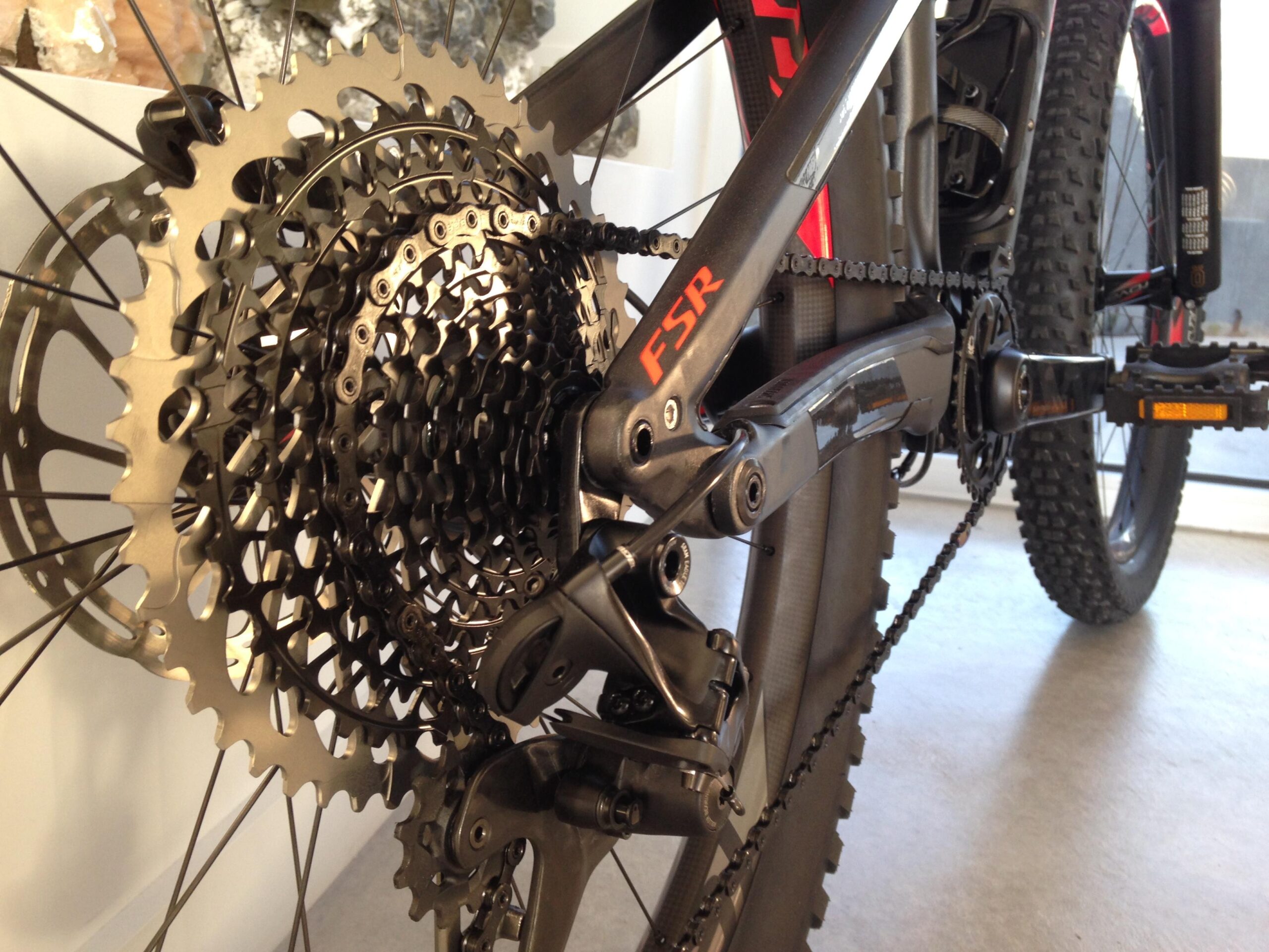 Specialized Stumpjumper FSR 6Fattie: Close-up of a mountain bike's drivetrain, showcasing the gears, chain, and derailleur. The components are metallic and detailed, emphasizing the intricate design of the gearing system. The bike frame is partially visible in the background, highlighting its modern construction.