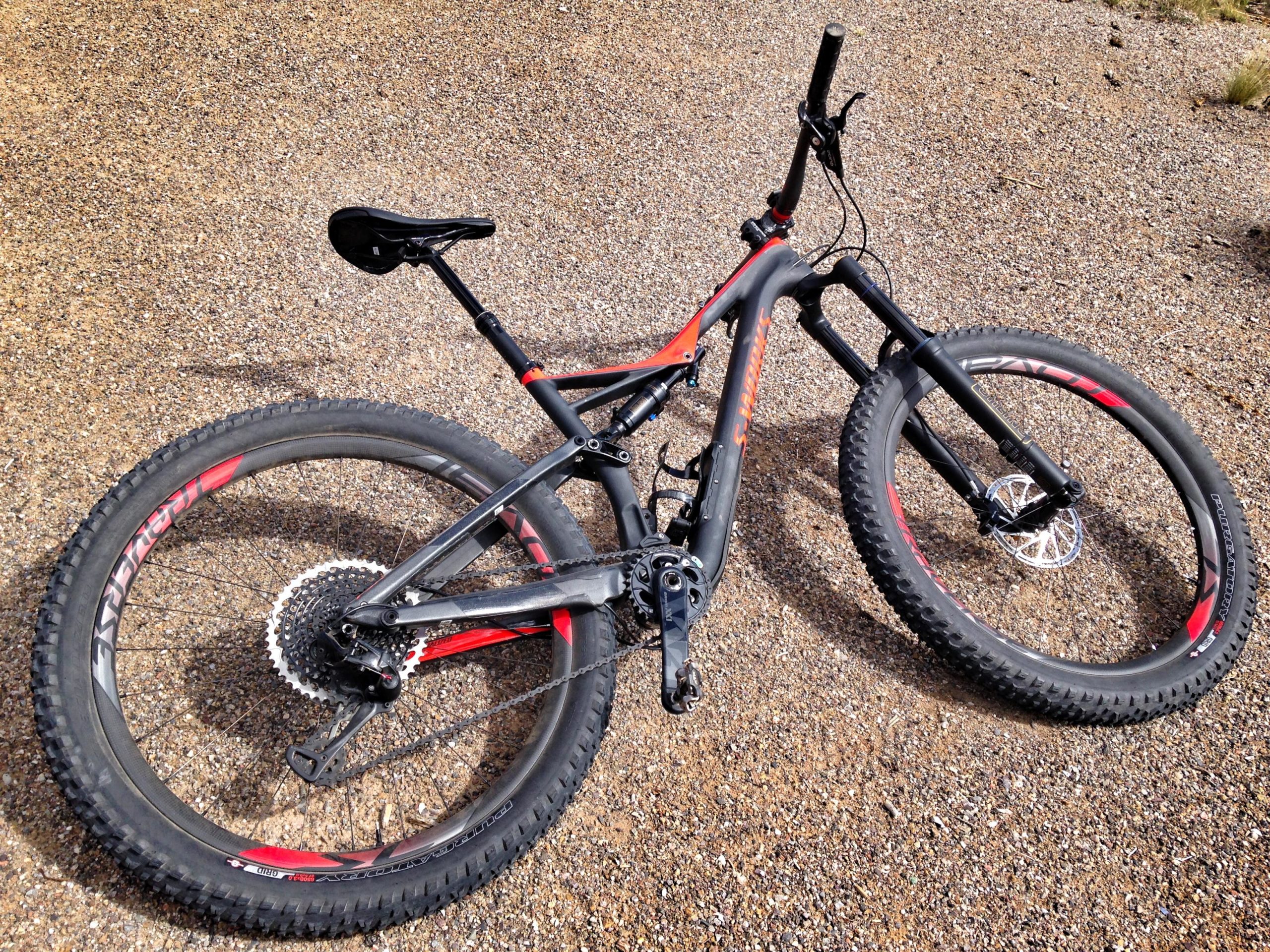 A mountain bike with a black and red frame, lying on a gravel surface. The bike features thick tires, a single rear gear, and a front suspension fork. Mariposa Fat Bike Trails mountain bike trail.