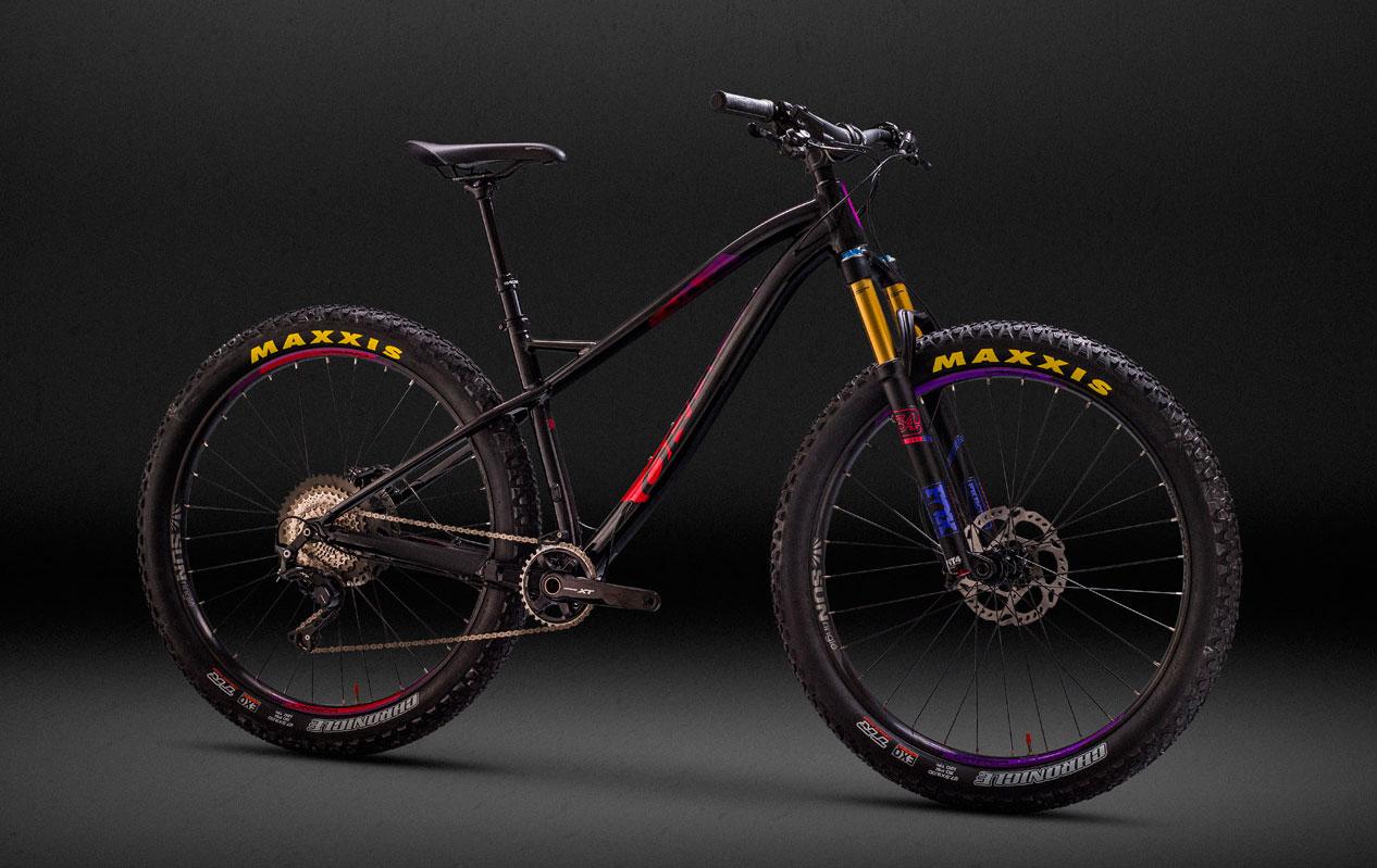 Orbea Loki: A high-performance mountain bike displayed against a dark background. The bike features a sleek black frame with vibrant accents, a prominent front suspension fork, and rugged tires labeled "MAXXIS." The drivetrain includes a visible cassette and chain, showcasing its advanced components.