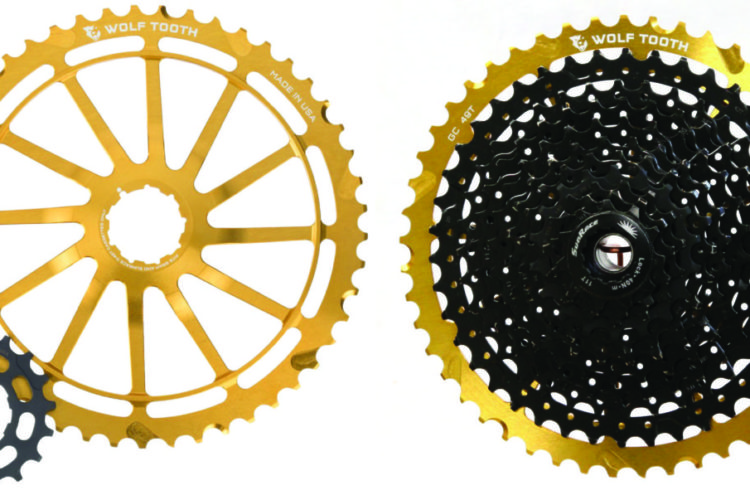 A gold-colored bicycle sprocket with 49 teeth is displayed on the left, alongside a black cassette featuring numerous gears, also marked with "GC 49T" and the brand name "Wolf Tooth." Both components are part of a bike's drivetrain system.