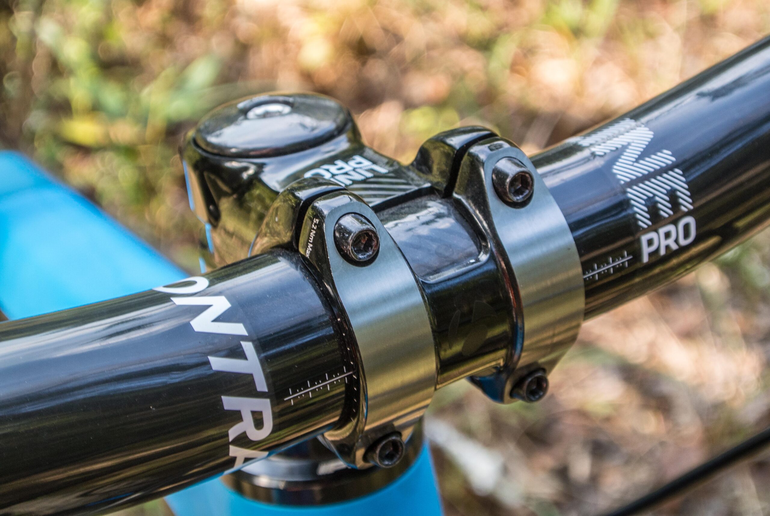 Trek Remedy 9: Close-up view of a bike's handlebar stem, featuring a black metal stem clamp and handlebars with contrasting graphics. The background includes greenery, suggesting an outdoor setting.