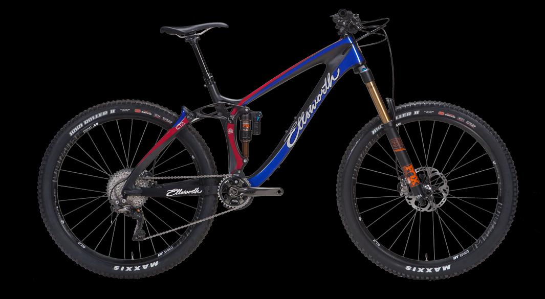 Ellsworth Rogue Forty: A mountain bike featuring a sleek design with a blue and red color scheme. It has a carbon frame, front suspension with a gold fork, and wide tires suitable for off-road terrain. The bike is displayed against a black background.
