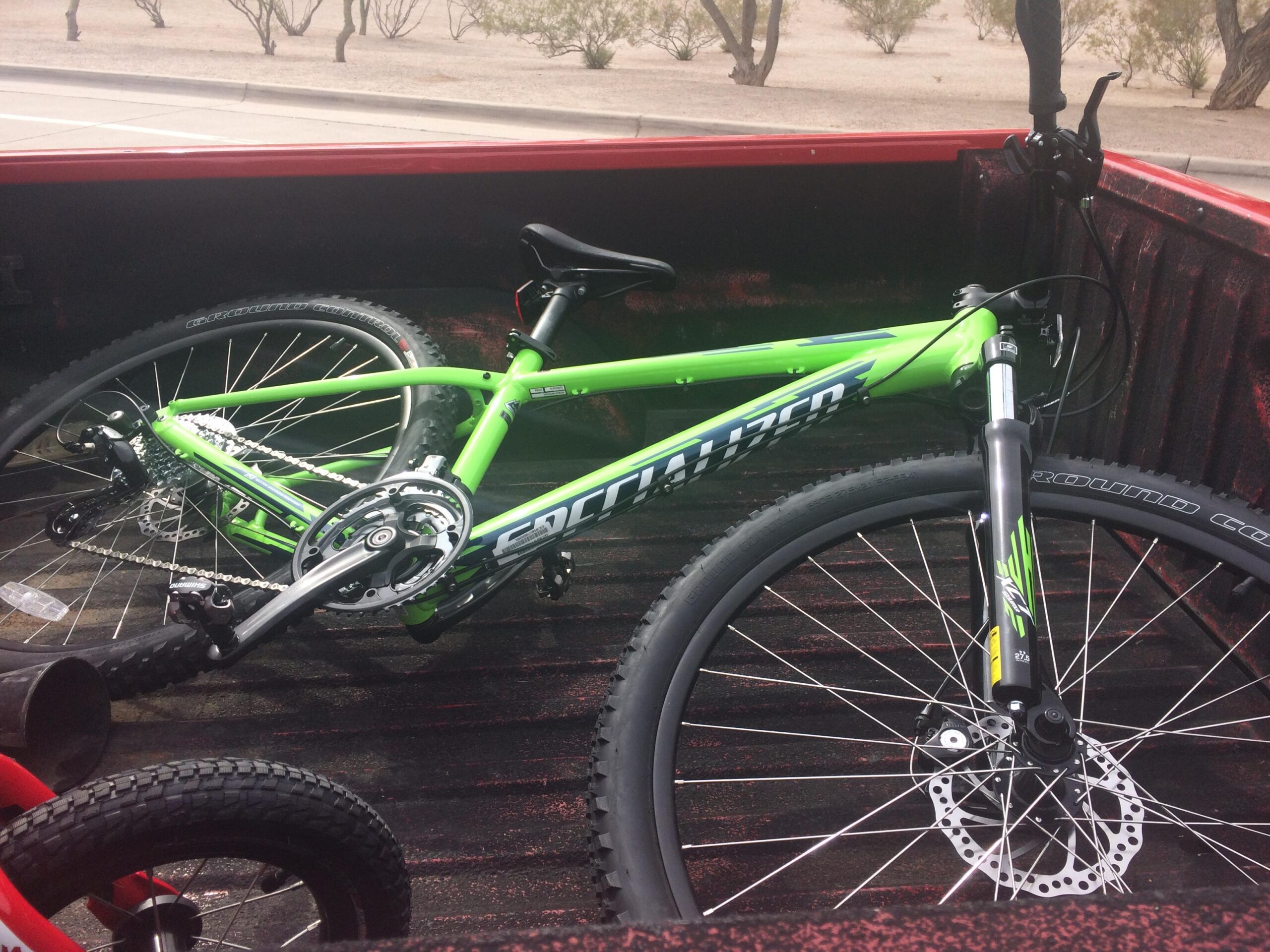 Specialized Pitch 650b: A green mountain bike resting in the bed of a red pickup truck, with a view of a desert landscape in the background. The bike features thick tires and a disc brake system.
