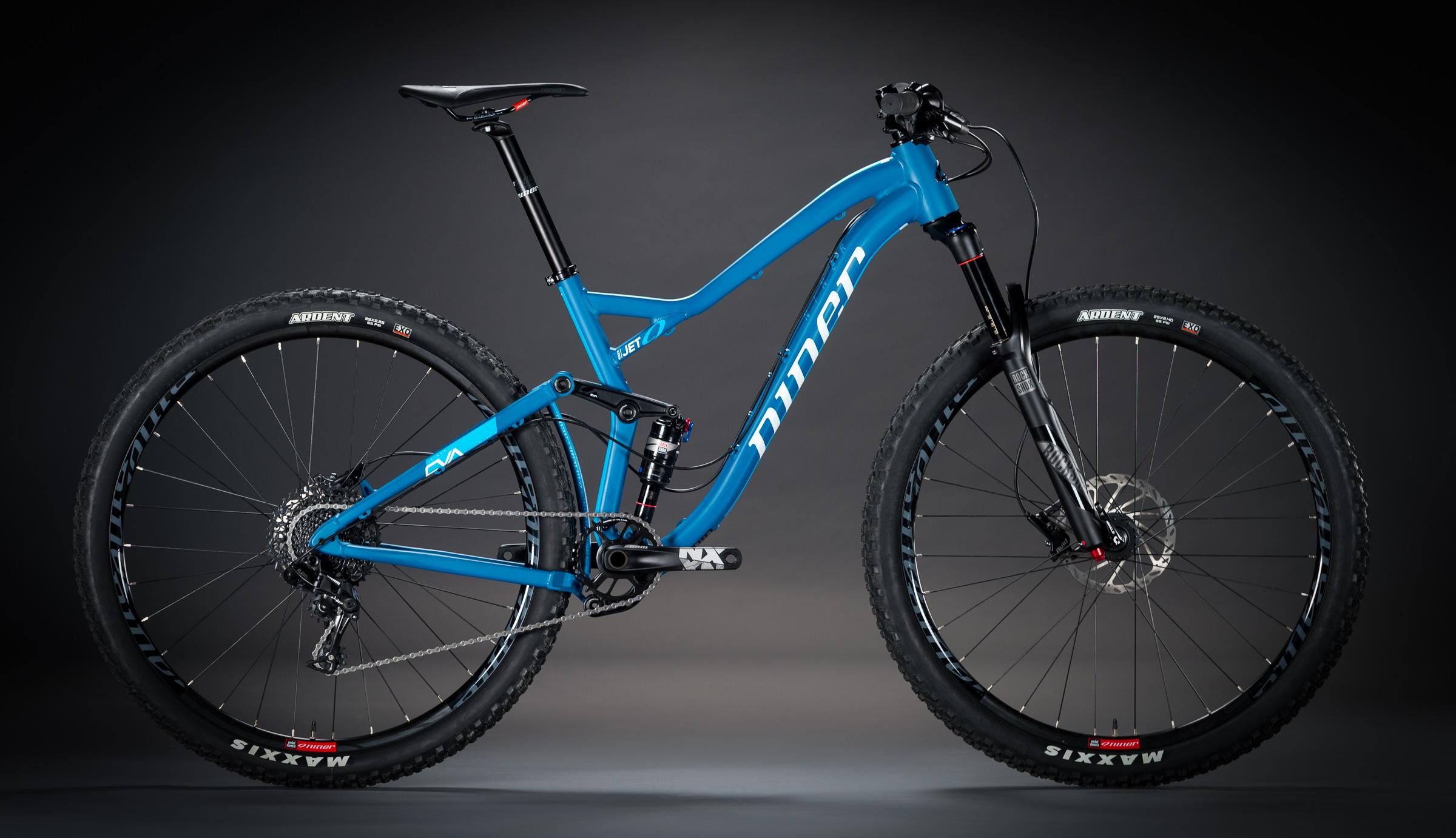 Niner Jet 9: A blue mountain bike with a sleek design, showcasing a lightweight frame and advanced suspension system. The bike features high-performance tires and a modern gearing system, positioned against a dark background to emphasize its sporty appearance.