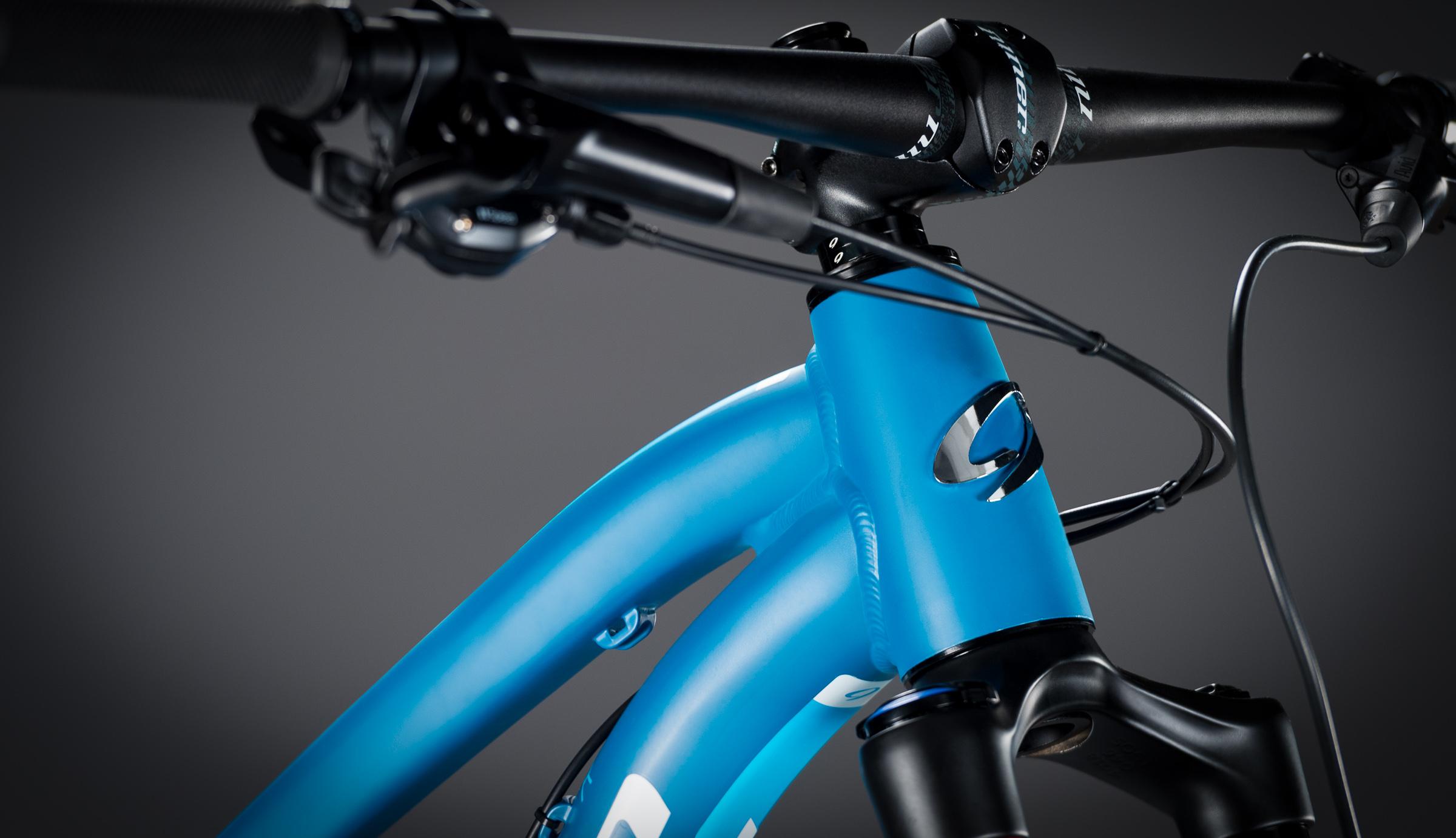 Niner Jet 9: Close-up of a blue mountain bike frame, showcasing the front fork, handlebars, and brake cables against a dark background.
