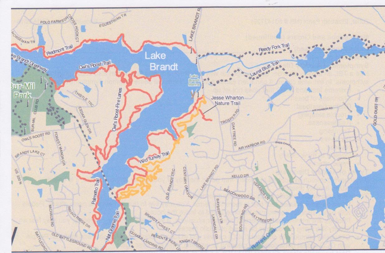 A map of Lake Brandt and surrounding trails, featuring marked pathways including the Owl's Roost Trail, Wild Turkey Trail, and Jesse Wharton Nature Trail. The map identifies nearby parks and includes road names for orientation. Wild Turkey mountain bike trail.