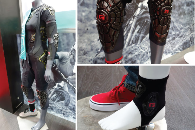A mannequin displaying a full-body protective suit designed for sports, featuring molded knee and arm pads. The suit is predominantly black with bright accents. Close-up views highlight the protective gear's details, including padded knee guards and ankle supports, alongside a vibrant red sneaker worn by the mannequin. The background features imagery of mountain biking, emphasizing the suit's intended use for action sports.