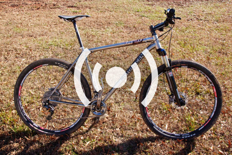 Alt text: A silver mountain bike with black tires and colorful rims is positioned on a grassy area. The bike has a suspension fork and a sleek design, showcasing its lightweight frame.