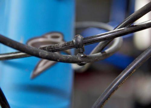 Jagwire Cable Rotating S Hooks: Close-up of bicycle cables intertwined with a plastic cable tie, set against a blurred background of a blue bicycle frame.