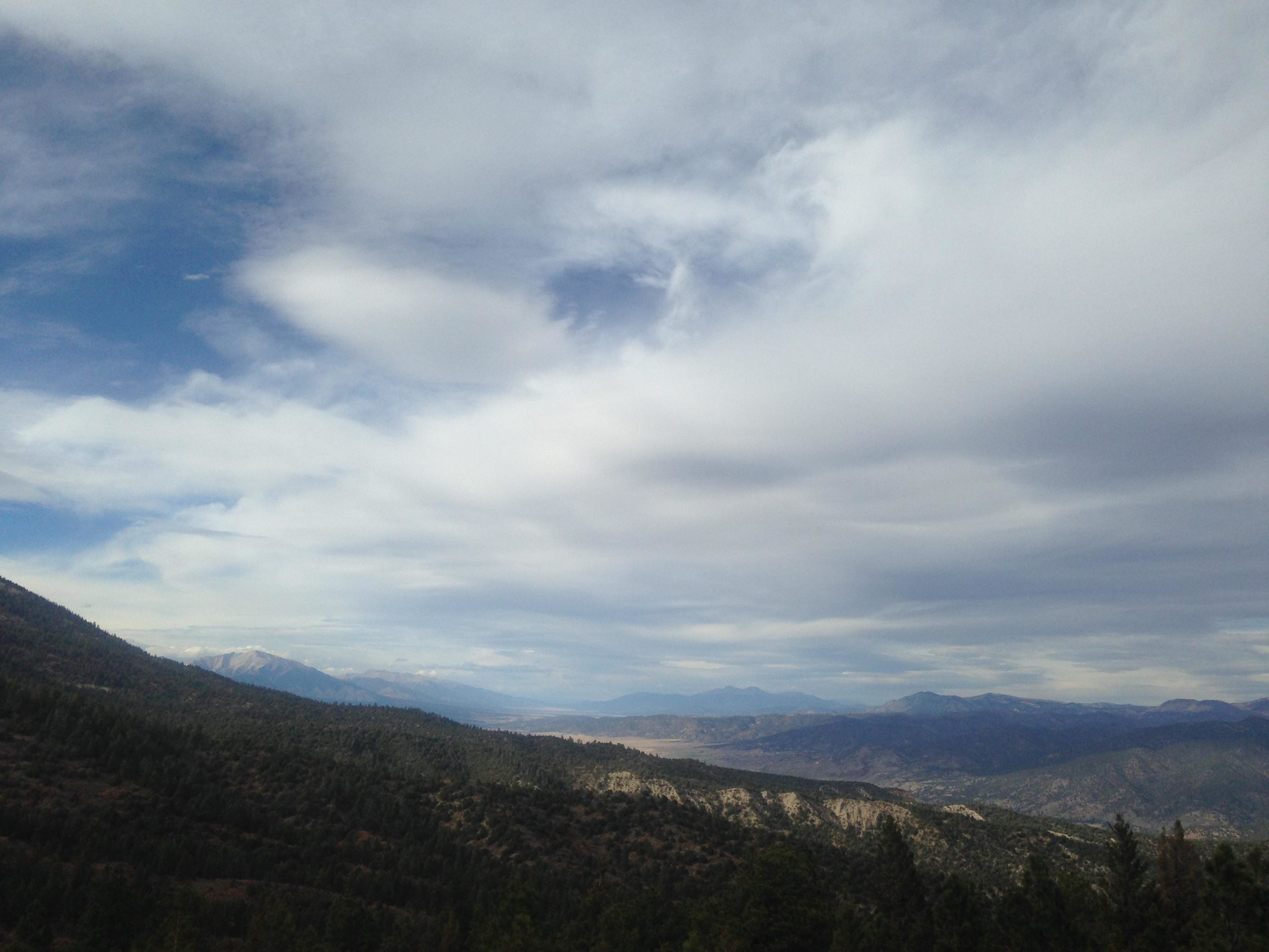 A panoramic view of rugged mountains and lush green forests under a cloudy sky. The landscape features rolling hills and valleys, with distant peaks visible on the horizon, creating a serene natural scene. Rainbow Trail: Methodist Mountain Thd to Bear Creek Thd mountain bike trail.