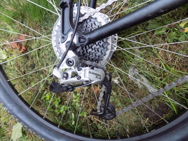 Motobecane Motobecane 529 HT: Close-up image of a bicycle's rear derailleur and cassette, featuring a SRAM X4 component, set against a grassy background. The focus is on the gears and chain of the bike.