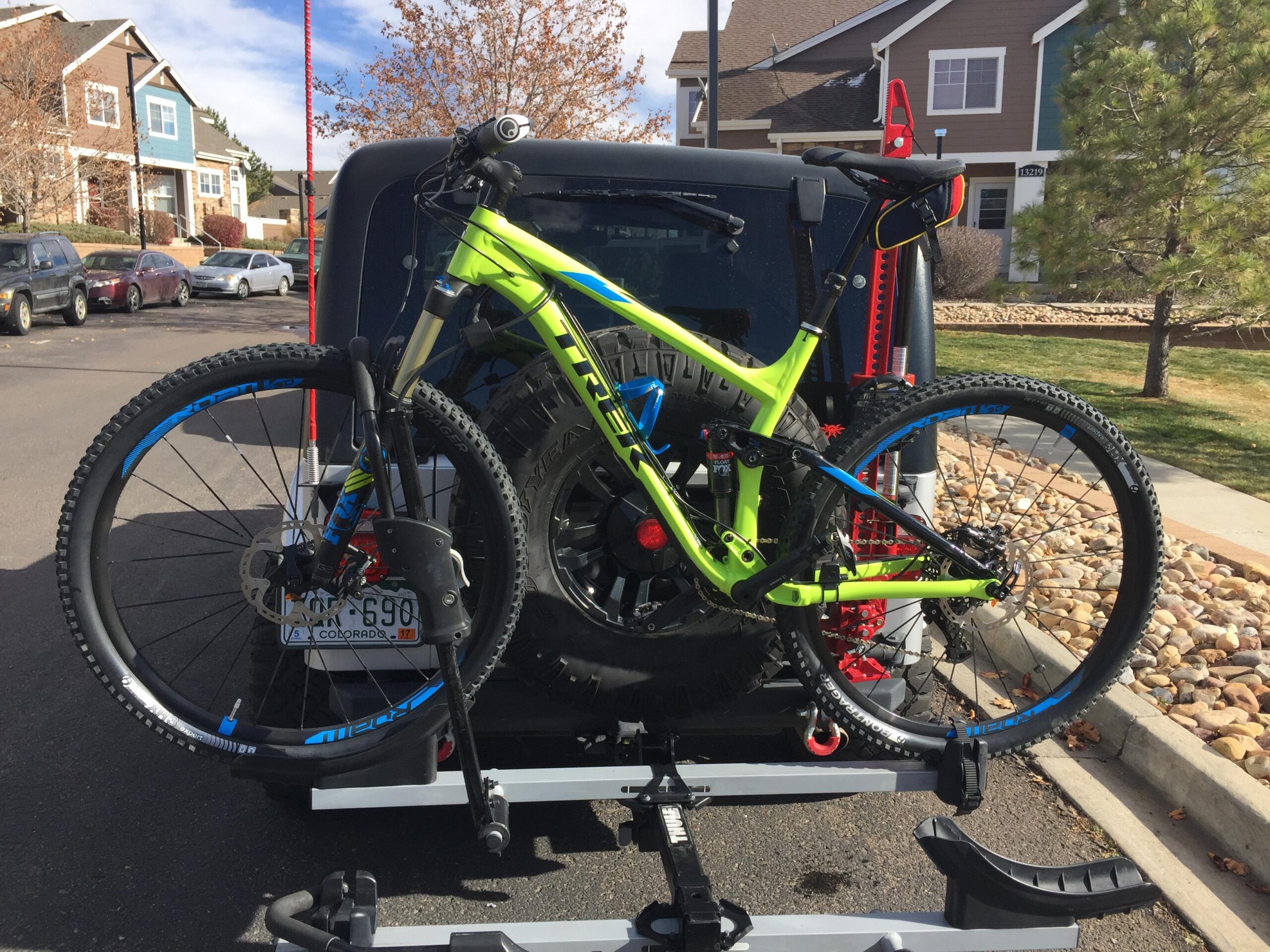 Trek Fuel EX 9 29: A bright green mountain bike mounted on the back of a vehicle, with a clear blue sky and suburban houses in the background. The bike features large tires and a modern design, securely attached to a bike rack.