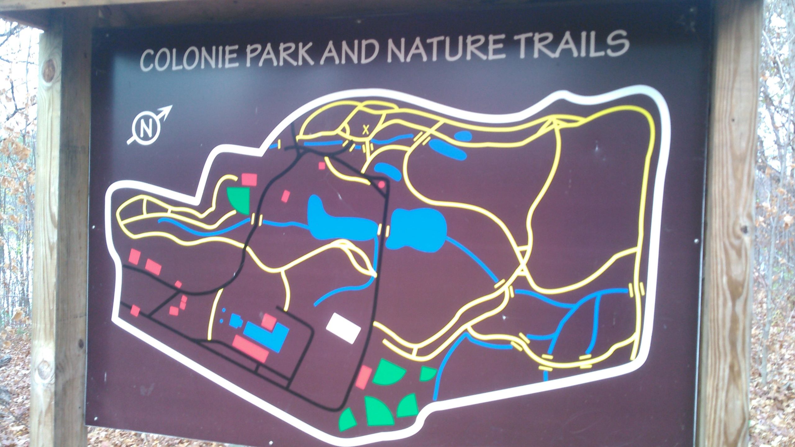 Map of Colonie Park and Nature Trails, featuring highlighted paths, water bodies, and designated areas marked in various colors against a brown background. North is indicated at the top, and key landmarks are outlined for navigation. Colonie Town Park/Ridge Trail mountain bike trail.