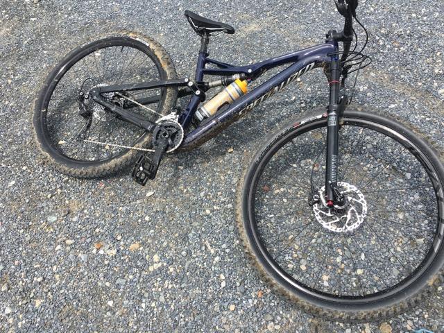 Specialized Stumpjumper FSR Comp Carbon 29: A mountain bike lying on gravel terrain, featuring a dark frame and a visible water bottle mounted on the frame. The bike's wheels show signs of off-road use, with dirt and debris.