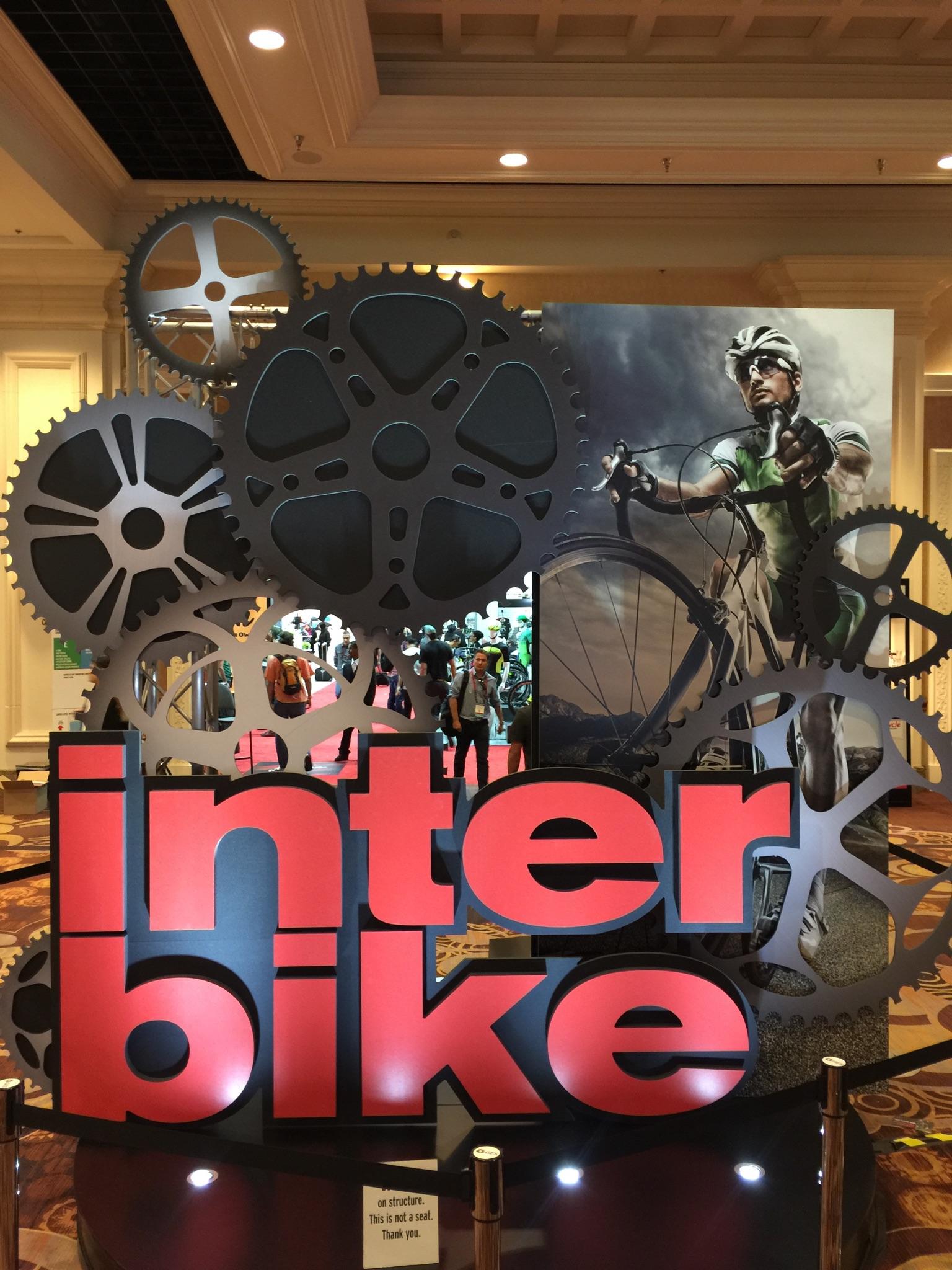 Specialized Stumpjumper: Alt tag: "Sign for Interbike featuring large red letters surrounded by bicycle gears, with a backdrop of a cyclist and an exhibition space in the background."