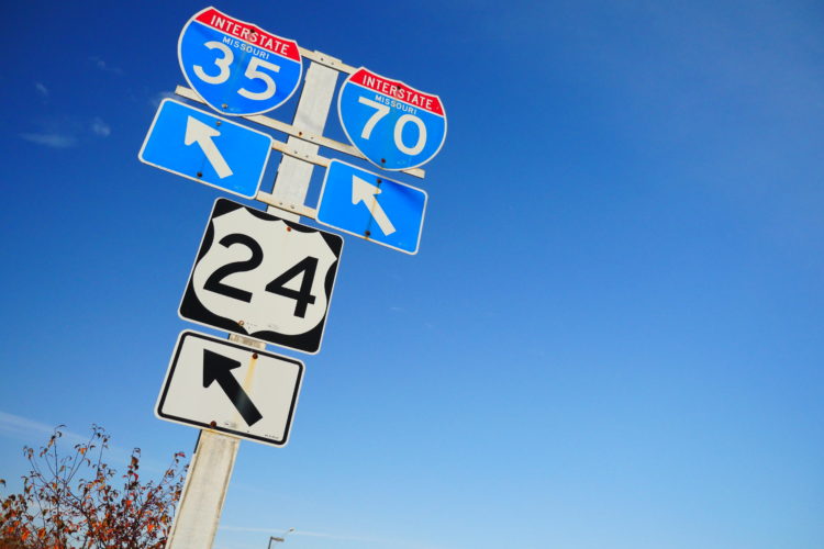 A road sign displaying Interstate 35 and Interstate 70 with directional arrows, along with a separate sign for Highway 24, against a clear blue sky.