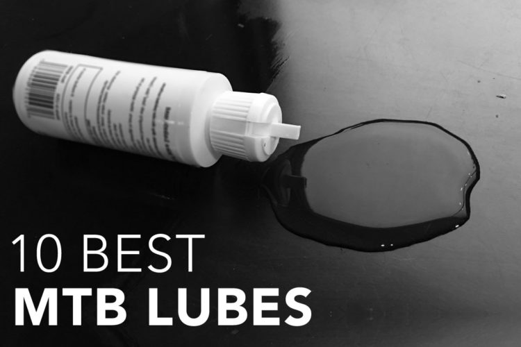 A bottle of mountain bike lubricant lying on a reflective surface with a small puddle of oil beside it. The text "10 Best MTB Lubes" is displayed prominently in the lower section of the image.