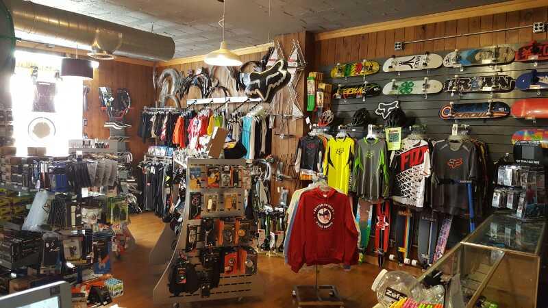 Interior of a sports shop featuring a variety of motocross and skateboarding gear. The walls display an assortment of clothing, helmets, and accessories, while racks showcase skateboards and other sports equipment. The shop has a cozy atmosphere with wooden paneling and bright lighting.