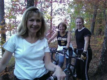 Specialized SWORKS Stumpjumper FSR: Three women on mountain bikes in a forested area during autumn, surrounded by colorful fall foliage. One woman is smiling in the foreground, while the other two are positioned behind her, dressed in casual athletic clothing.