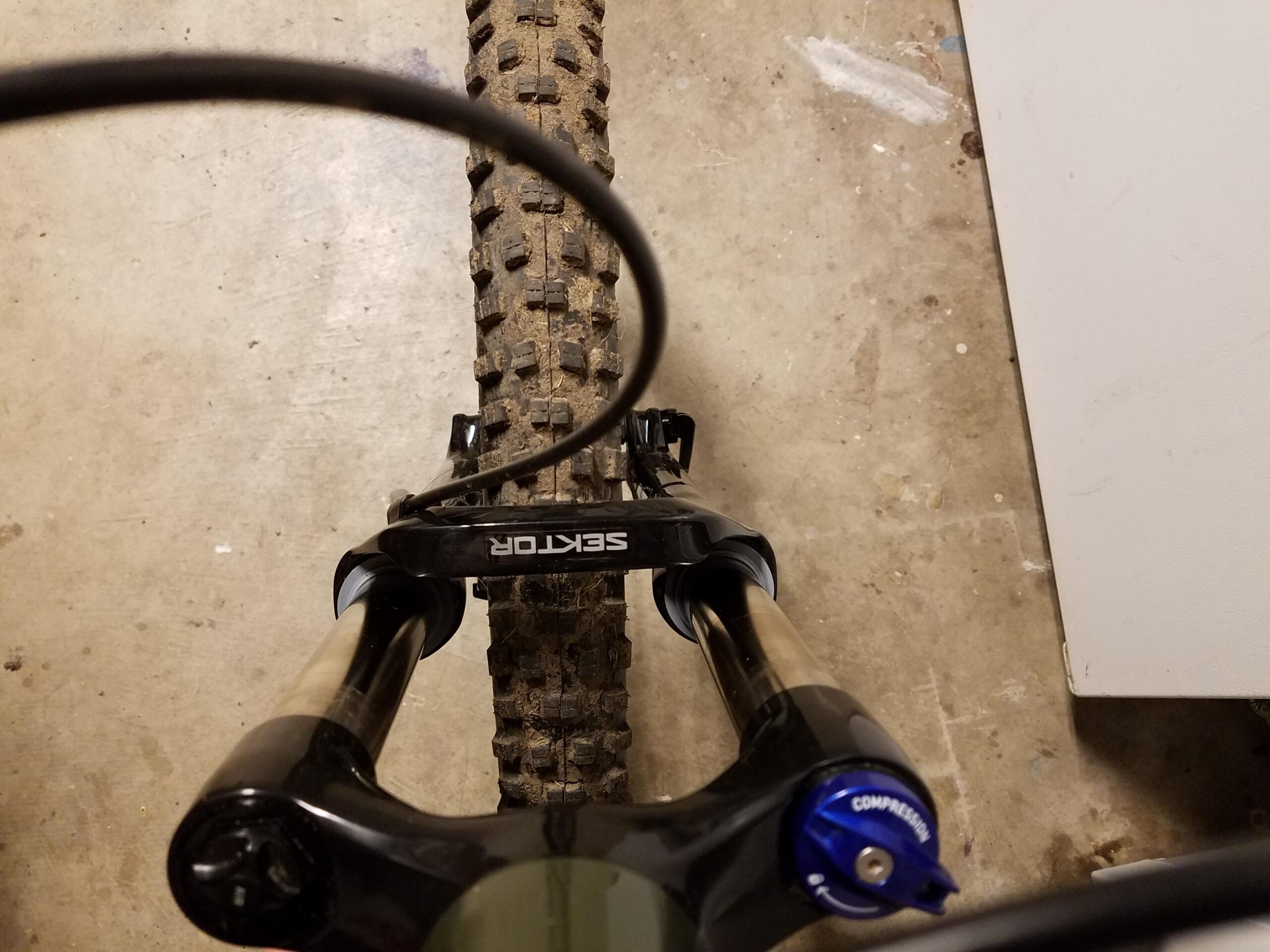 Fuji Fuji Reveal 1.1: Close-up view of a mountain bike's front fork and tire, showcasing the suspension component labeled "SEKTOR" and a muddy tire tread, set against a concrete background.