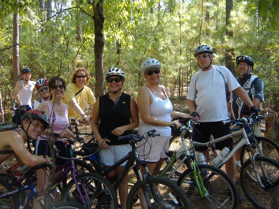 Specialized SWORKS Stumpjumper FSR: Group of nine people posing with mountain bikes in a wooded area, wearing helmets and casual clothing, enjoying a sunny day outdoors.