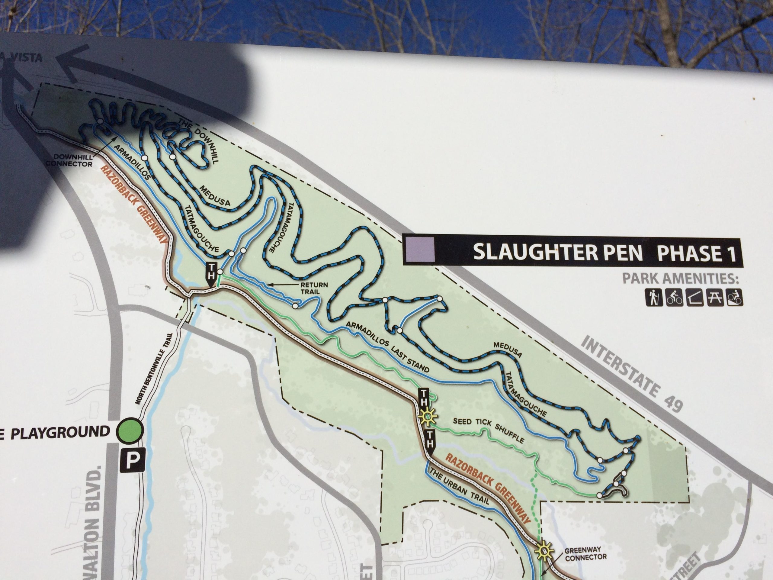 Map overview of Slaughter Pen Phase 1, displaying various trails such as "The Downhill," "Medusa," and "Seed Tick Shuffle." Features indicate park amenities for walking, biking, and other activities, along with nearby roads and access points. Slaughter Pen Trail mountain bike trail.