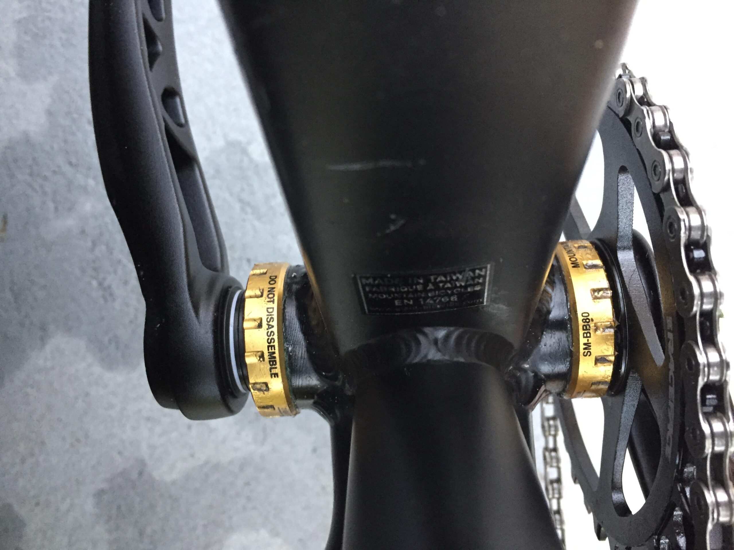 Giant Talon 29er: Close-up view of a bicycle's bottom bracket area, featuring a black crank arm and a gold bearing adjustment cap with the label "DO NOT DISASSEMBLE." The surrounding components include a black chainring and chain.